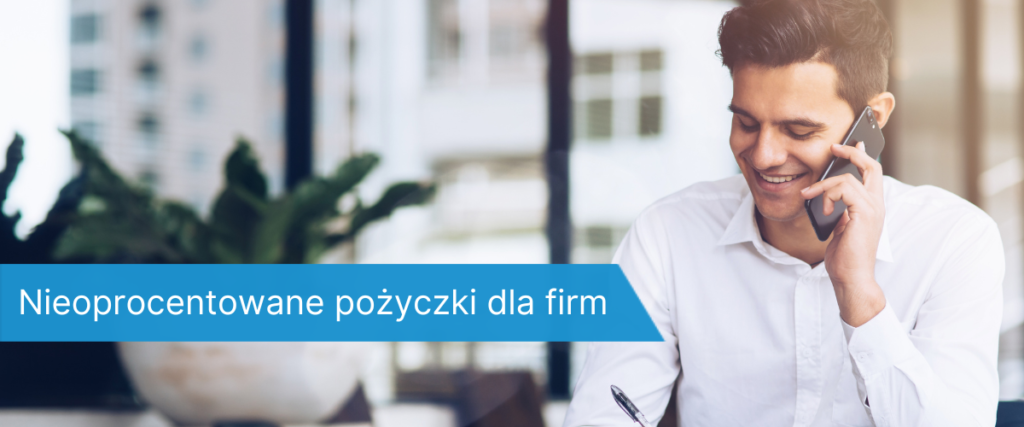 Młody mężczyzna w białej koszuli, siedzący przy biurku i rozmawiający przez telefon, w tle biurowe okno i roślina